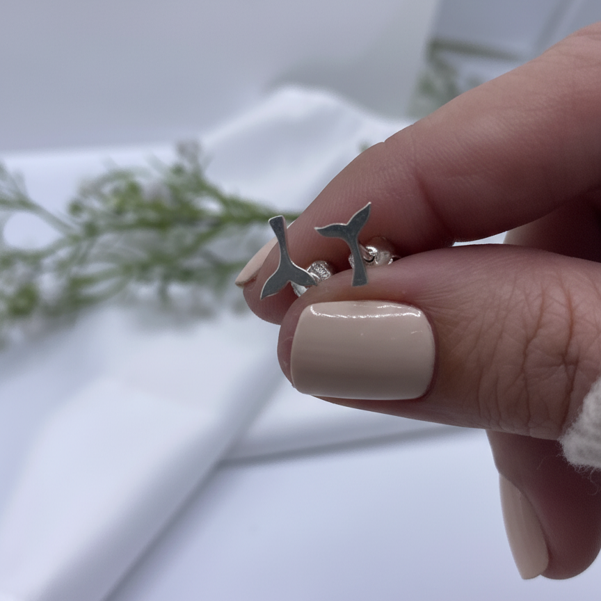 Luisana Jewelry Mini Whale Tail Studs held in hand with a neutral nail polish against a soft background