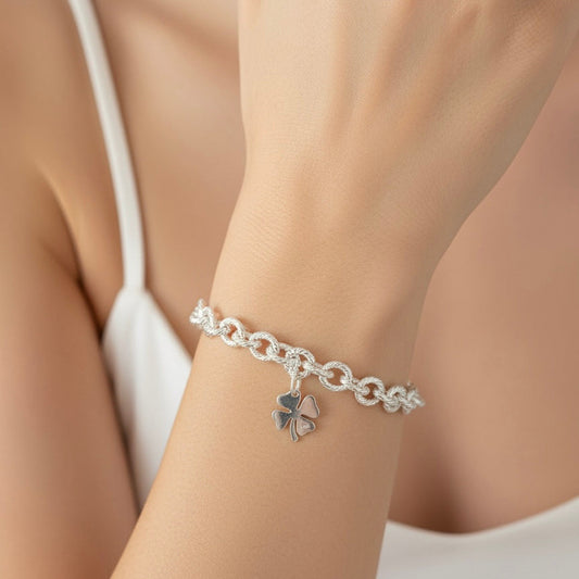Silver chain bracelet with a clover charm on a wrist against a neutral background