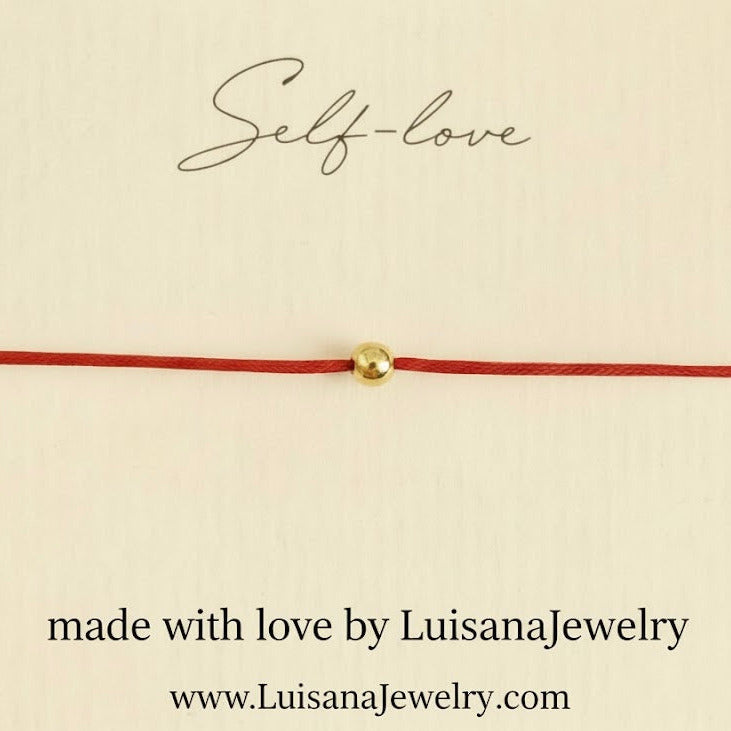 Red cord bracelet with a gold bead on a beige background, featuring 'Self-love' text and LuisanaJewelry branding.