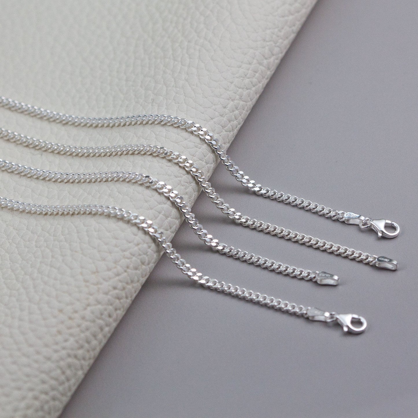Four silver Cuban Chain 1.4mm necklaces with lobster clasp closures displayed on a textured surface