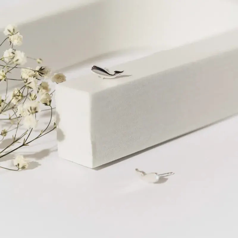 Mini Whale Studs from Luisana Jewelry on a clean surface with delicate flowers