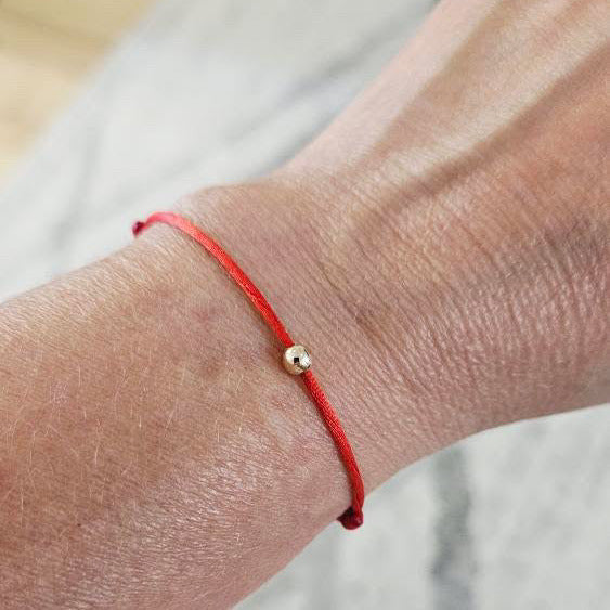 Red string bracelet on a wrist with a gold bead against a neutral background